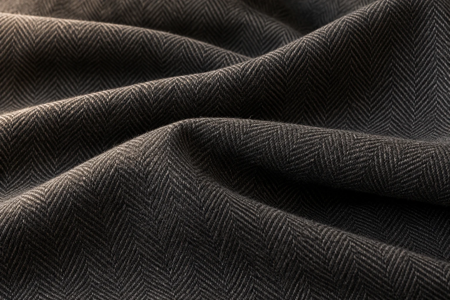 Illustrative close-up of charcoal herringbone wool cloth in soft folds